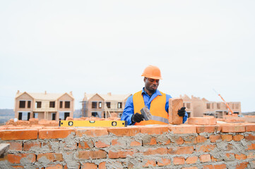 African american Bricklayer industrial worker installing brick masonry on exterior wall with trowel...