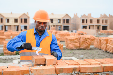 African american construction worker. Portrait of mason bricklayer installing red brick with trowel...
