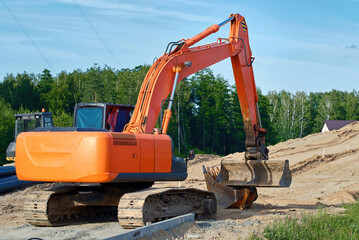 Tracked excavator working on suburban road construction project, preparing foundation for new...