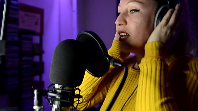 Female singer wearing headphones recording song in professional studio