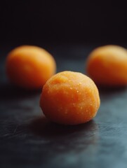 Three orange sweets on a black surface, likely candied fruits or dessert balls.