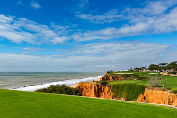 Scenic coastal golf course in Vale do Lobo, Portugal, with lush green fairways atop rugged orange...