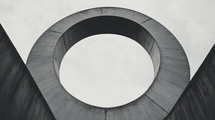 Fototapeta premium Abstract concrete structure with a large circular opening against a cloudy sky.