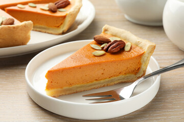 Piece of tasty homemade pumpkin pie with seeds and nuts on wooden table, closeup