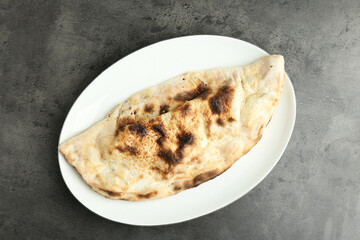 One delicious calzone on grey textured table, top view
