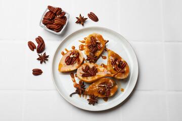 Delicious pears with caramel sauce, pecan nuts and anise stars on white tiled table, top view