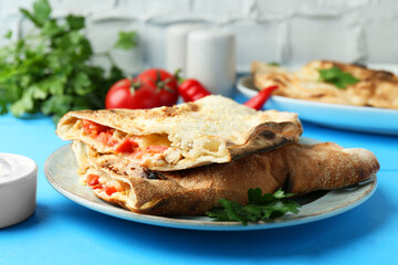 Halves of tasty calzone with meat, cheese, tomato and sauce on light blue table, closeup