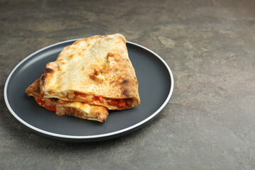 Halves of tasty calzone with meat, cheese and tomato on grey textured table, closeup. Space for text