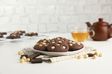 Tasty chocolate cookies with hazelnuts and tea on white table