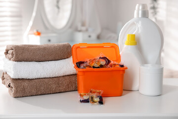 Laundry capsules, detergents and clean towels on white table in bathroom