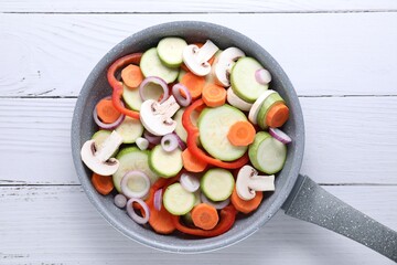 Frying pan with mix of fresh vegetables and mushrooms on white wooden table, top view