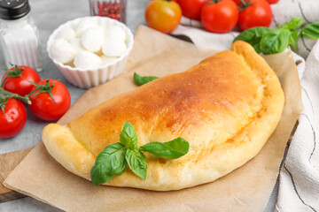 Tasty vegetarian calzone with tomatoes, mozzarella cheese and basil on grey table, closeup