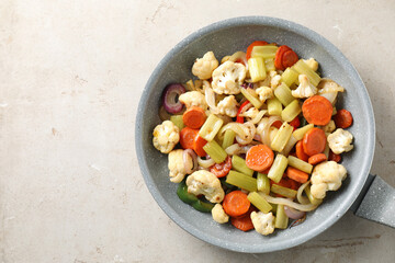 Frying pan with vegetables on light textured table, top view. Space for text