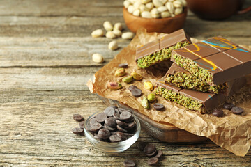 Pieces of Dubai chocolate bar with pistachios, knafeh and cacao chips on wooden table, closeup. Space for text