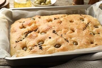 Delicious focaccia bread with olives and thyme in baking dish on table, closeup