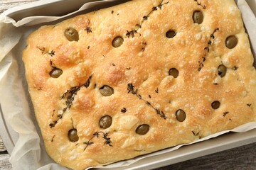 Delicious focaccia bread with olives and thyme in baking dish on wooden table, top view