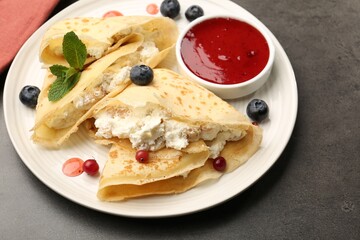 Delicious crepes with cottage cheese, jam, redcurrants and blueberries on grey table, closeup