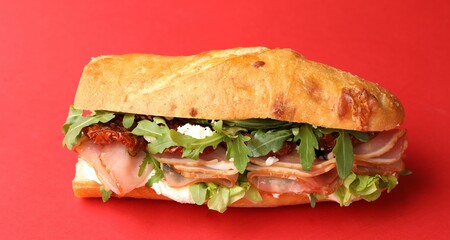 Baguette sandwich with ham and sun dried tomatoes on red background, closeup