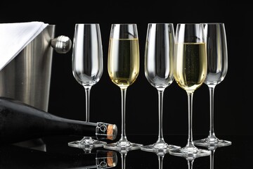 Bottle of sparkling wine, glasses and cooler bucket on black mirror surface