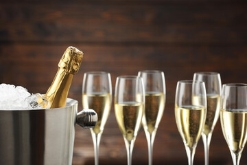 Bottle of sparkling wine in cooler bucket and glasses against wooden background, closeup