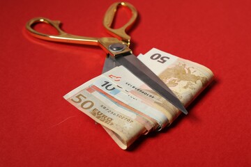 Euro banknotes and scissors on red background, closeup