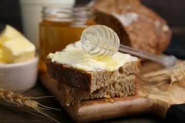Tasty sandwich with butter, honey and dipper on wooden table, closeup