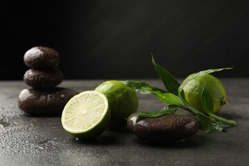 Spa composition with wet limes, pebble stones and bamboo leaves on grey table against black background, closeup