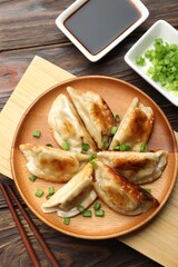 Delicious fried gyoza dumplings with green onions served on wooden table, flat lay