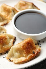 Fried gyoza dumplings with sesame seeds and soy sauce on table, closeup