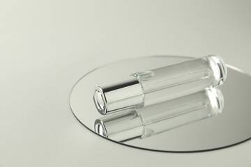 Bottle of serum and mirror on light background, space for text