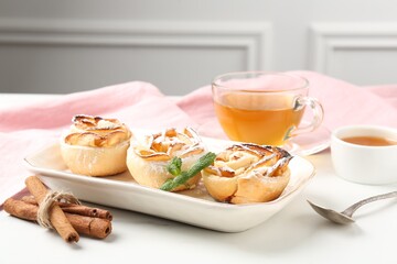 Freshly baked apple roses with mint, honey, cinnamon sticks and tea on white marble table, closeup