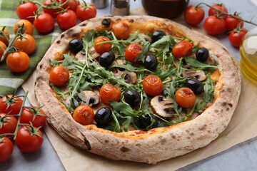 Tasty pizza with cherry tomatoes, black olives, mushrooms and arugula on grey table, closeup