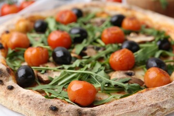 Tasty pizza with cherry tomatoes, black olives, mushrooms and arugula on table, closeup