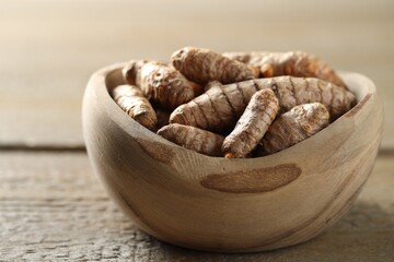 Raw turmeric roots in bowl on wooden table, closeup