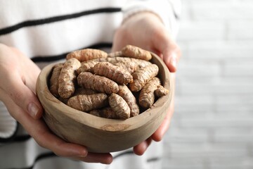 Woman holding bowl with raw turmeric roots on light background, closeup. Space for text