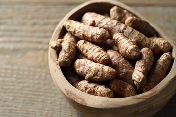 Raw turmeric roots in bowl on wooden table, closeup