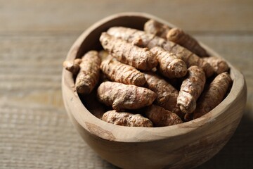 Raw turmeric roots in bowl on wooden table, closeup