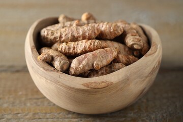 Raw turmeric roots in bowl on wooden table, closeup