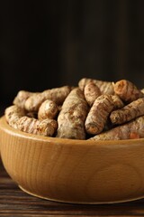 Tumeric rhizomes in bowl on wooden table, closeup