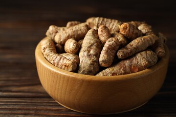 Tumeric rhizomes in bowl on wooden table, closeup