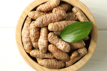 Tumeric rhizomes with leaf in bowl on white wooden table, top view