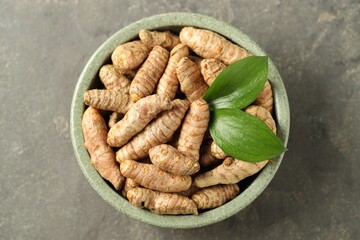 Tumeric rhizomes with leaves in bowl on grey table, top view