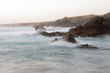 Fototapeta premium Long exposure of ocean waves crashing against rocks in Porto Covo, Portugal