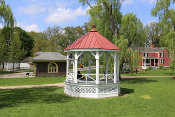 White Gazebo with Red Roof in a Green Park Surrounded by Trees and Historic Homes