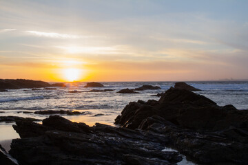 A breathtaking sunset over the ocean in Porto Covo, Portugal, with the warm golden light casting a tranquil glow over the water. The image captures the peaceful beauty of the coastline
