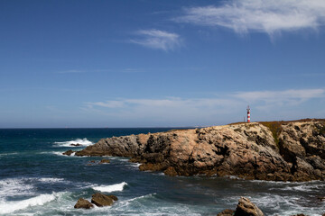 The iconic lighthouse in Porto Covo stands proudly on the edge of a dramatic cliff, overlooking the vast ocean. This stunning view along the Rota Vicentina trail captures the rugged beauty of Portugal