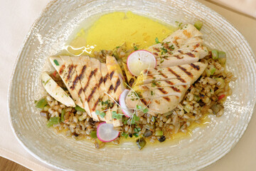 Grilled chicken breast sliced over a bed of pearl barley vegetables and a light yellow sauce