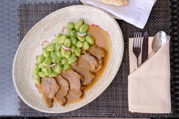 Sliced meat in a rich gravy served with green gnocchi and radish slices