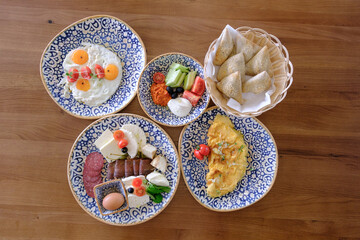A delicious and diverse breakfast spread featuring eggs cheese cured meats pastries and fresh vegetables
