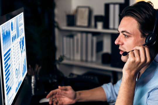 Call center consulting with customers on headphones on monitor in business paragraph with typing on pc with dynamic data marketing analysis planning at modern home office at night time. Pecuniary.